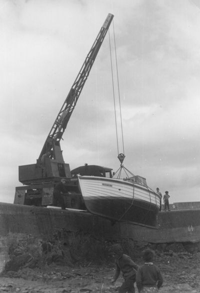 The crane lowers the boat, named 'Constancy', in to the inner harbour at low tide